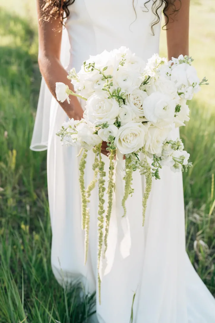 A white bridal bouquet of roses and stock with long strands of trailing amaranthus falling well below the stems.