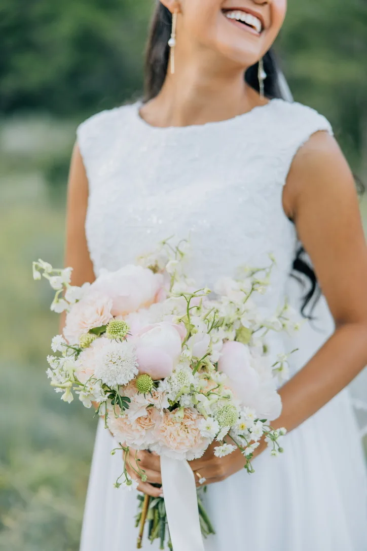 Close view of a bride holding a loose blush and white bouquet against a fitted ivory gown.